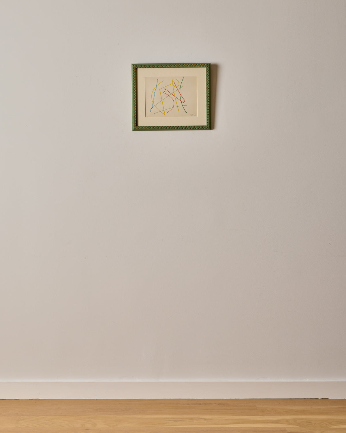 Framed artwork on a plain wall with a wooden floor.