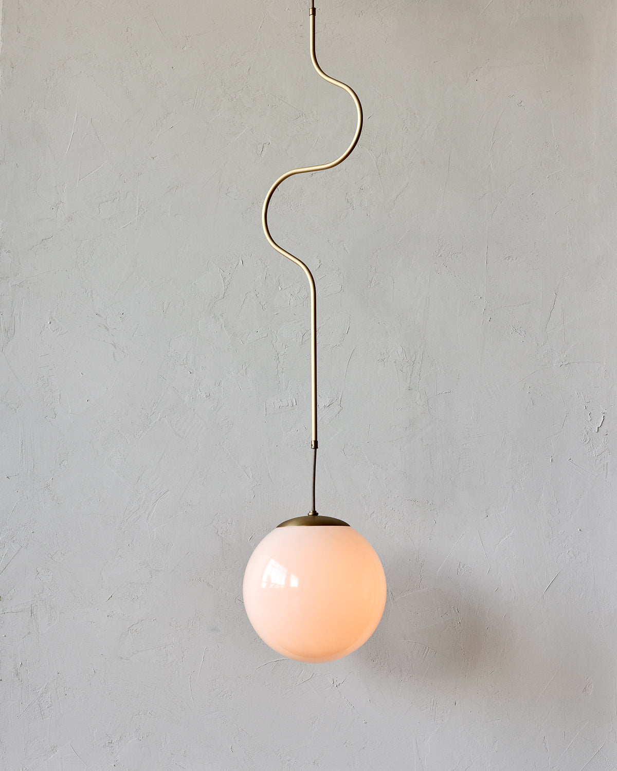 Modern brass globe pendant light with warm satin brass curved body and white milk glass globe