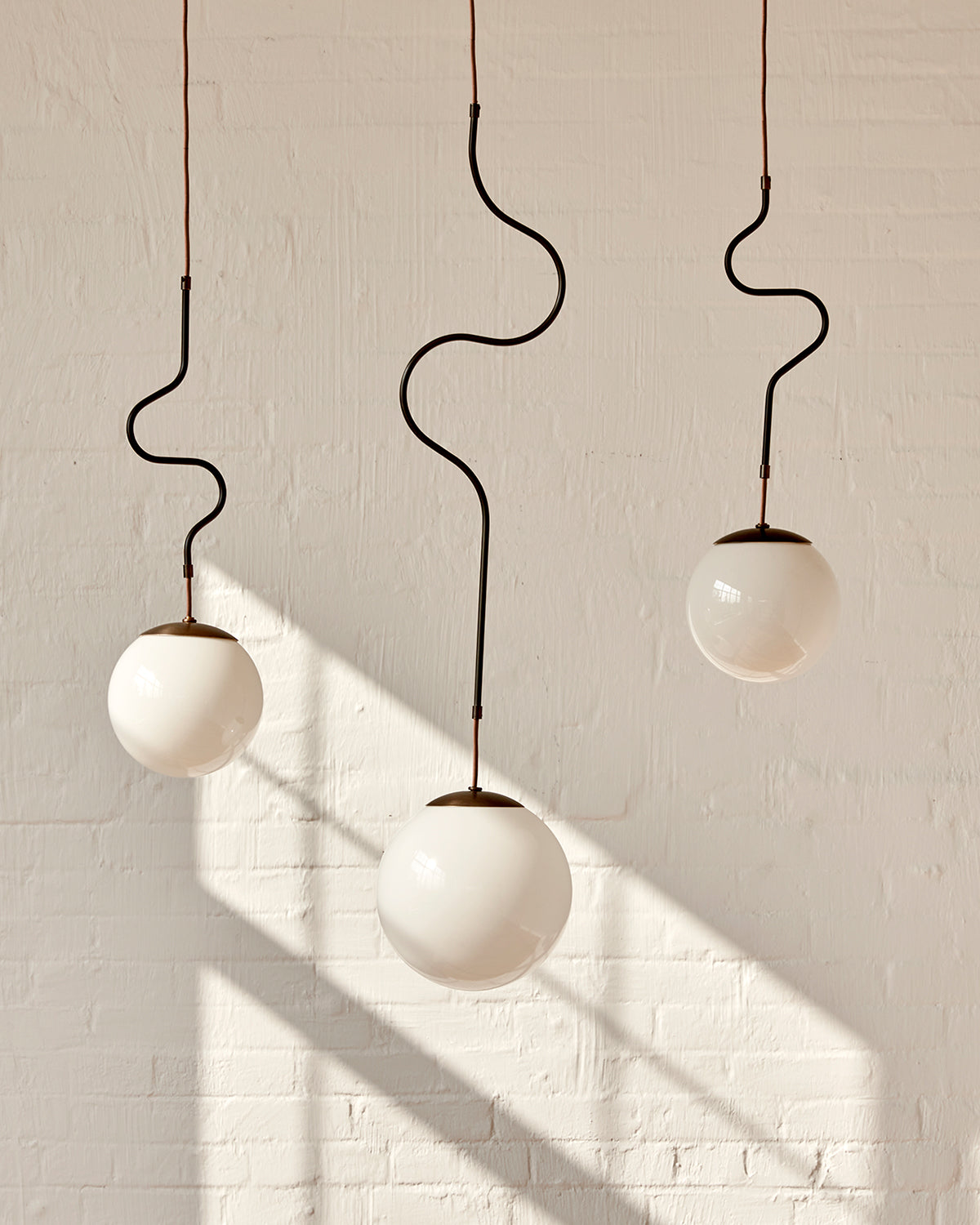 Modern black globe pendant light with dark oil rubbed brass curved body and white milk glass globe