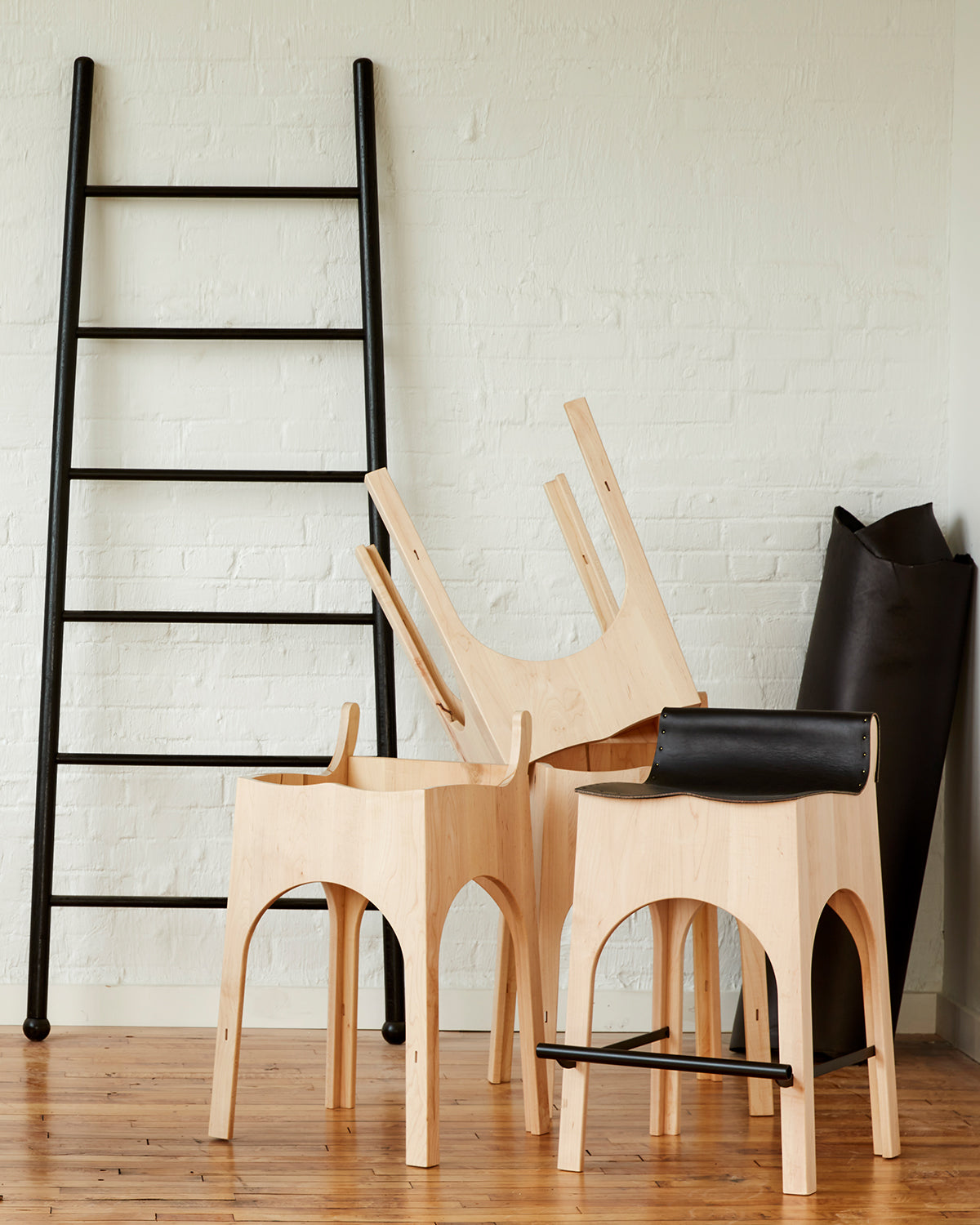 Sculpted stool with black leather and maple wooden base with metal foot rest and short backrest. Pictured with XL Wide Black Ladder. Counter and bar height. Handmade in Philadelphia by Lostine. Simple Interior Design. Warm American Modern Design