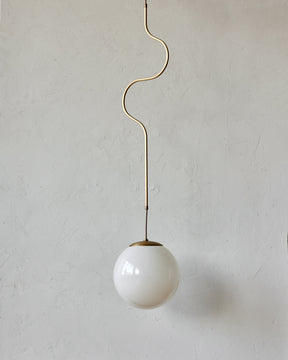 Modern brass globe pendant light with warm satin brass curved body and white milk glass globe