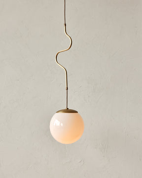 Modern brass globe pendant light with warm satin brass curved body and white milk glass globe